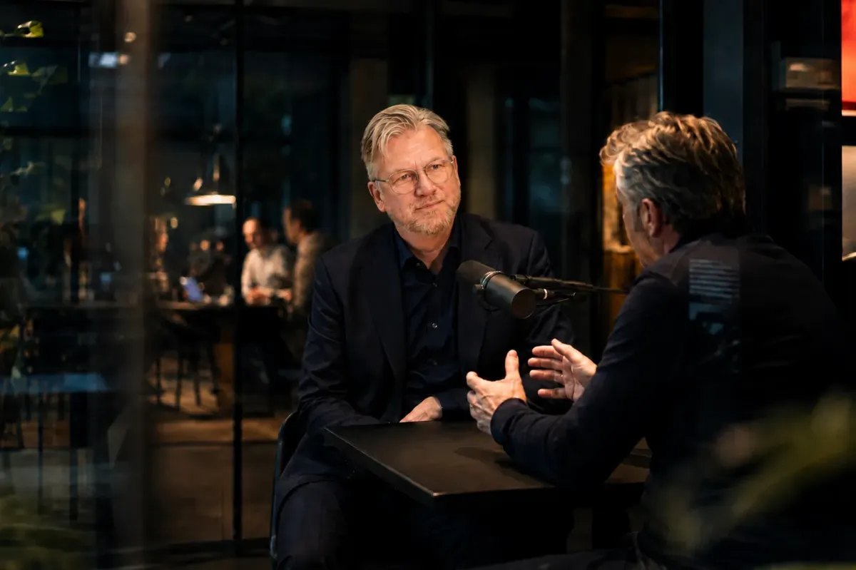 Twee mannen nemen een aflevering van Salesbazen op aan een statafel met een podcastmicrofoon ertussen